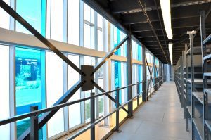 Vue intérieure d'une passerelle de mezzanine industrielle avec des étagères de rangement d'un côté et de grandes fenêtres de l'autre dans un entrepôt moderne