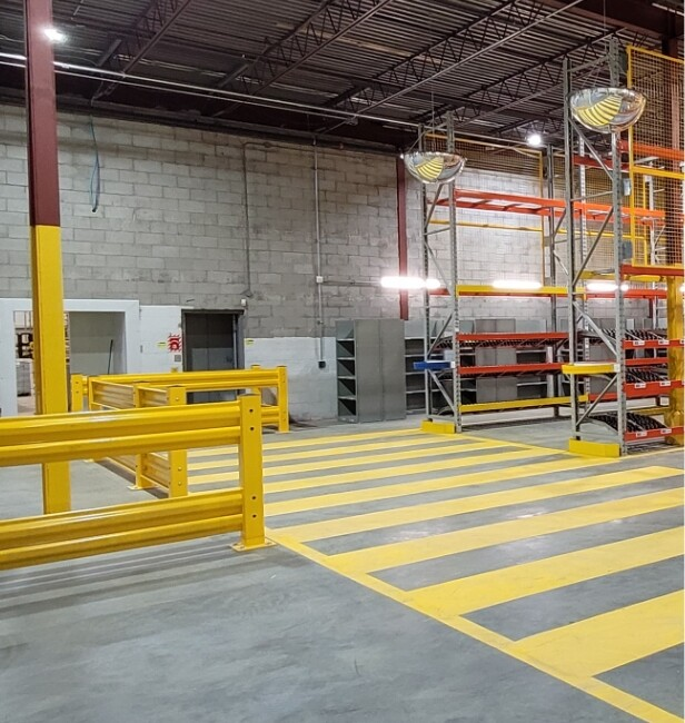 Heavy-duty safety guardrail system in an industrial warehouse with pedestrian floor markings and pallet racking
