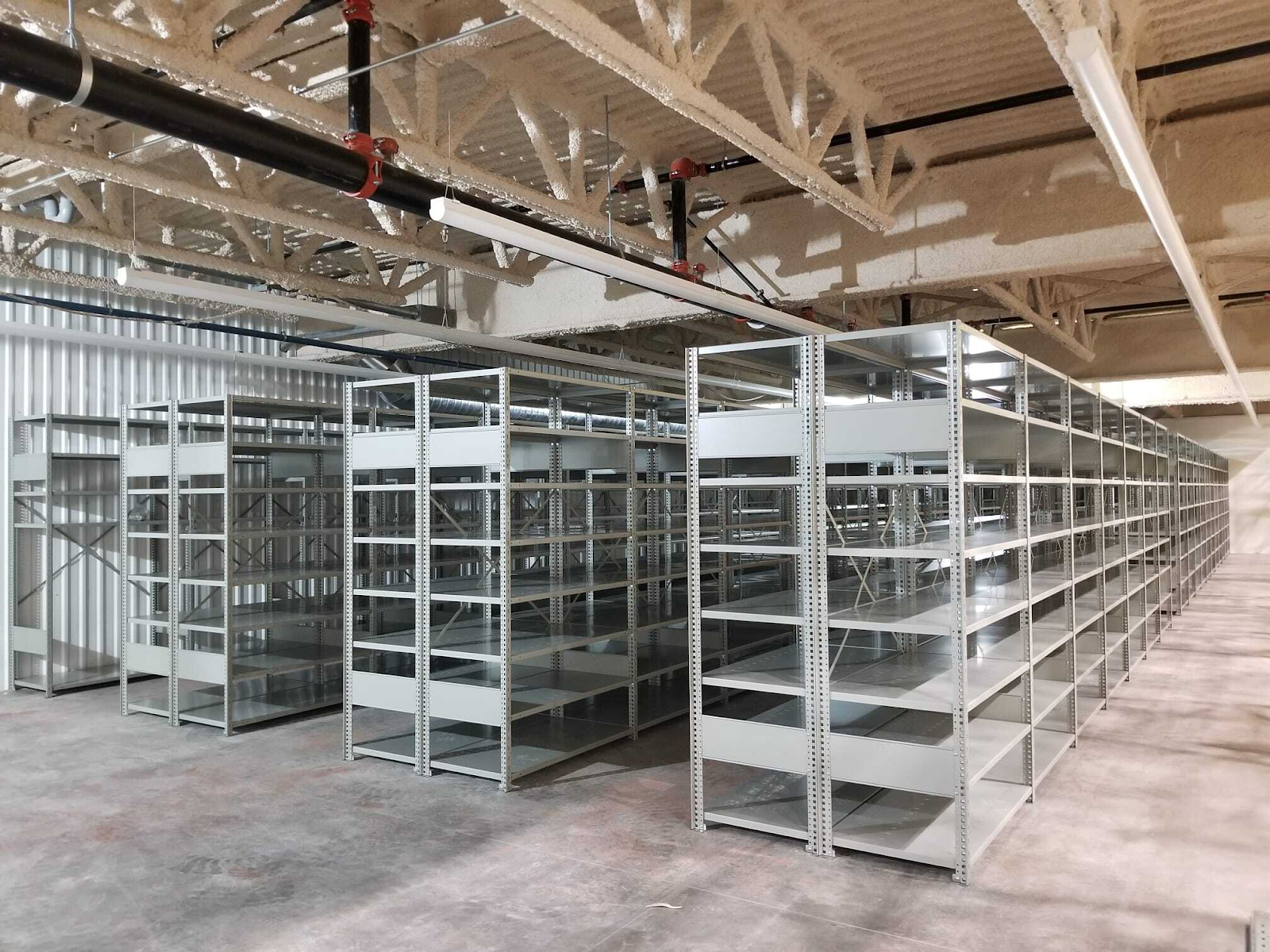Metal industrial shelves arranged in rows inside a warehouse storage area with open shelving units for efficient material organization