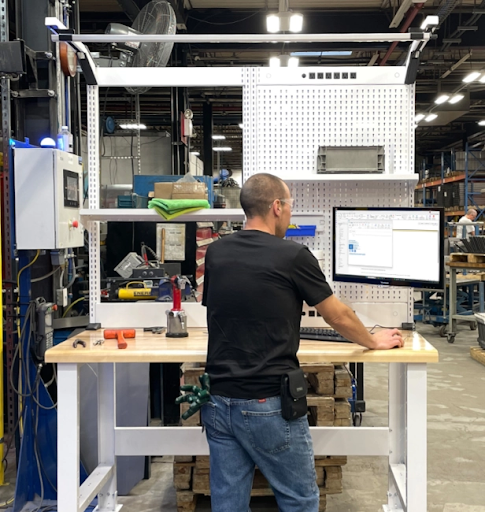 Industrial adjustable workbench with integrated storage and monitor in a manufacturing workspace, designed for ergonomic and efficient production tasks