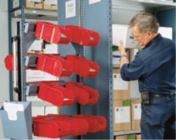 Warehouse workstation with red storage bins on metal shelving used by worker for parts organization and order picking.