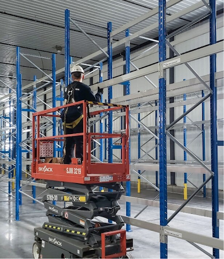 Technician installing warehouse racking system using a scissor lift in a clean industrial facility