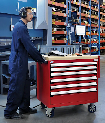 Technician using a red mobile tool cabinet with drawers in an industrial workshop equipped with warehouse shelving systems